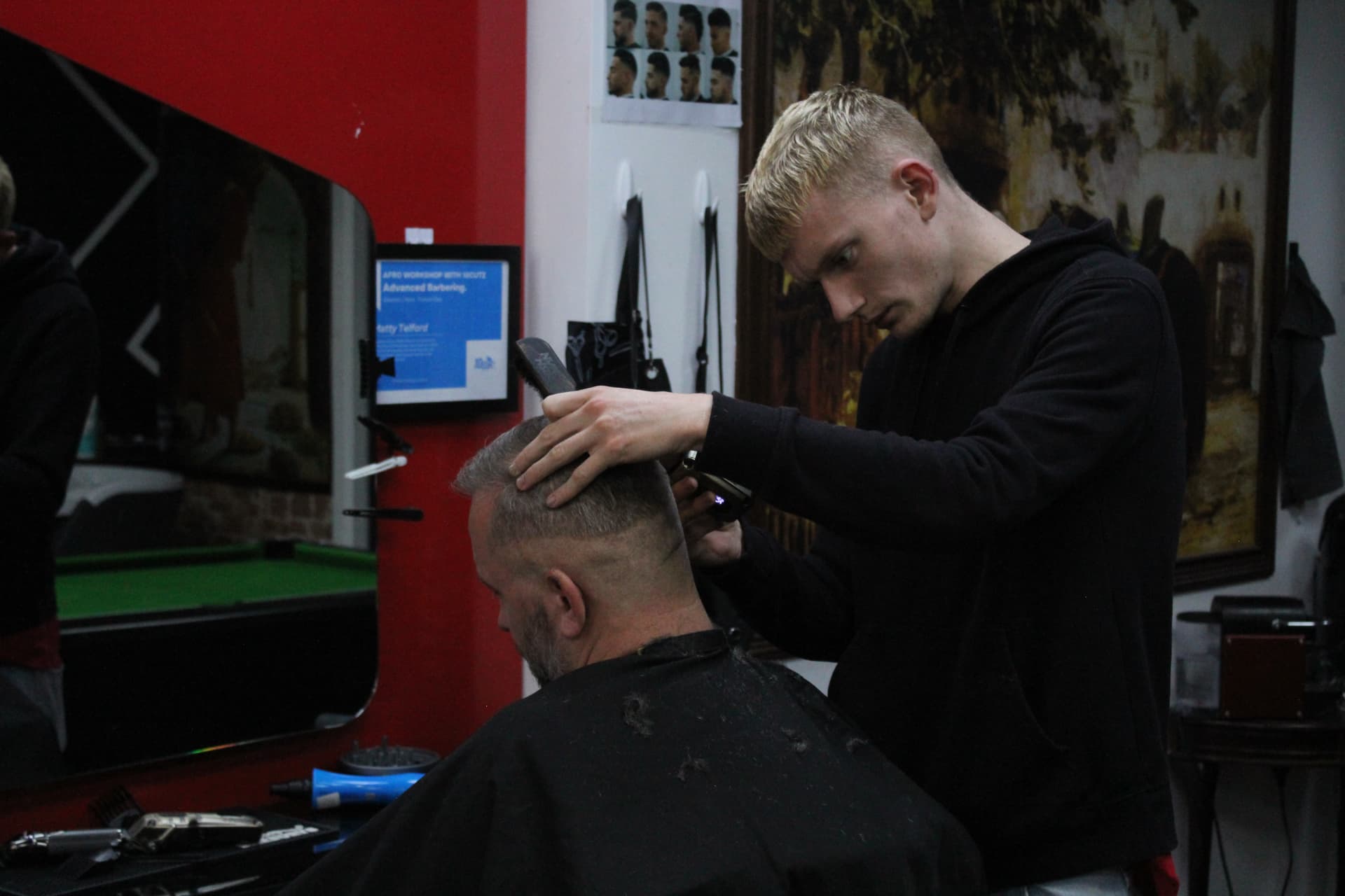 Barber at work inside City Barbers Cork with the pool table reflected in the mirror
